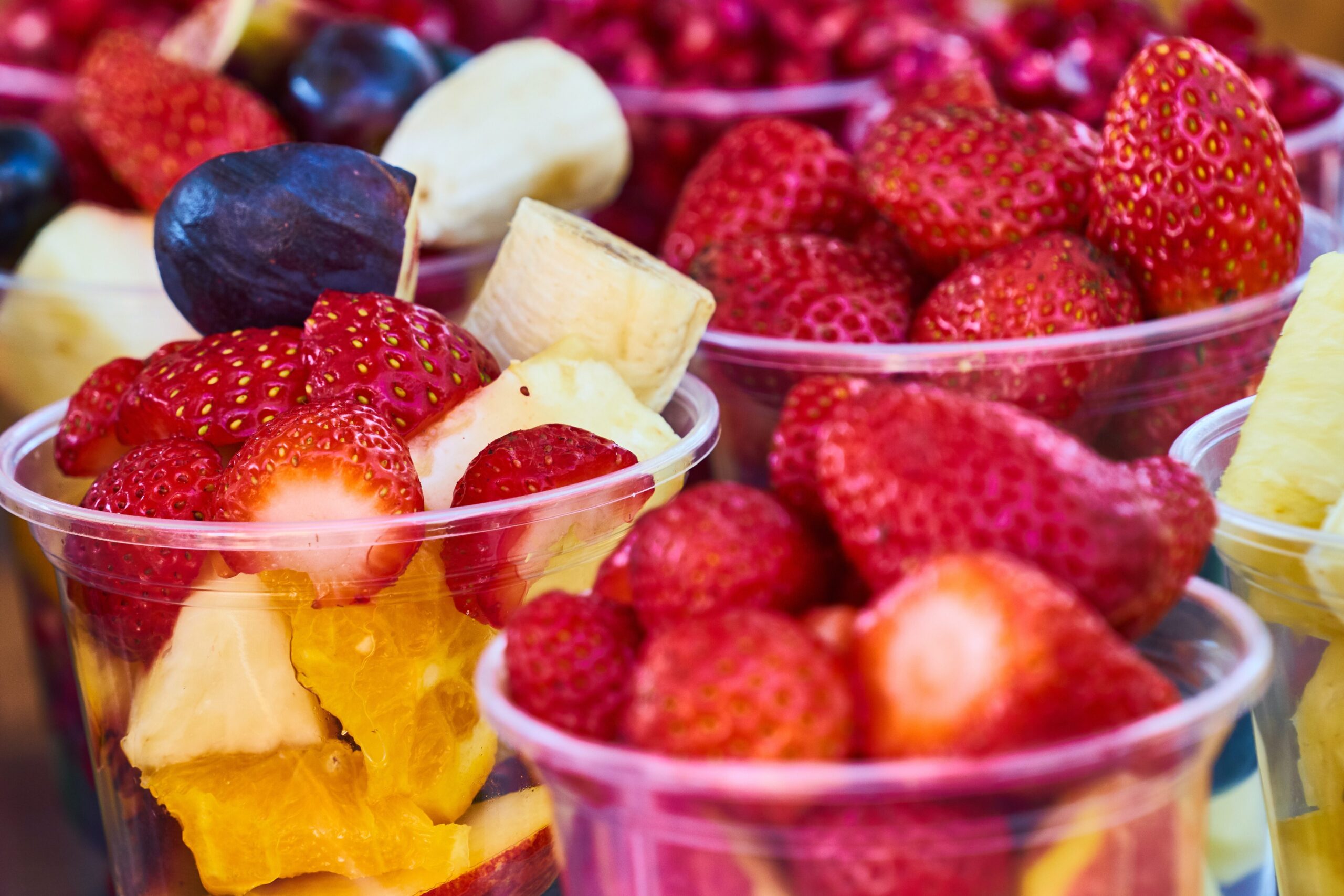 Nine clear plastic cups filled with bight summer fruit pieces with strawberries and blueberries on top